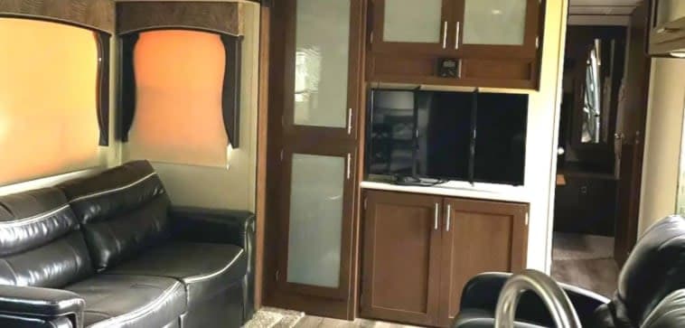 Spacious RV rental interior featuring a dark leather sofa, TV, and storage cabinets. Ideal for comfortable travel.