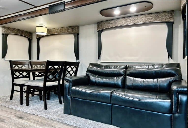Spacious and modern RV rental interior featuring a comfy black leather couch, dining area, and large windows. Perfect for travel!