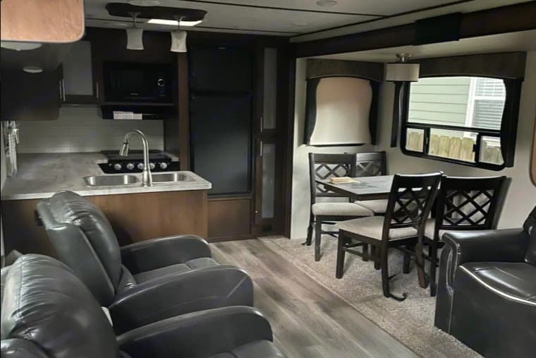 This RV rental's interior boasts a complete kitchen, dining table with chairs, and comfortable recliners in the living area.