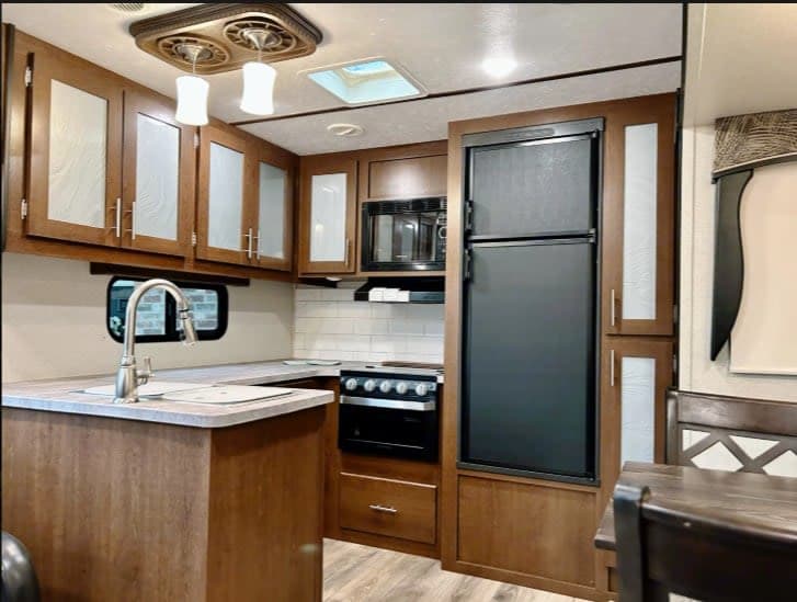 This rv rental offers a functional kitchen with wood cabinets, sink, stove, microwave, a black refrigerator, and dining area.