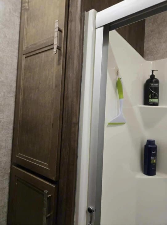 This RV rental bathroom features dark wood cabinets and a shower with shampoo, body wash, and a squeegee for easy cleanup.