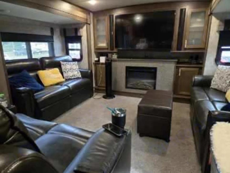 Comfortable RV rental living space featuring leather sofas, large TV, and electric fireplace for cozy travels.