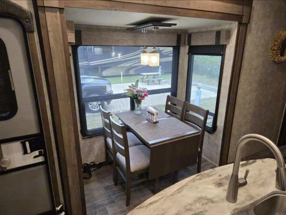 RV rental: Interior dining space with table, chairs, and scenic window views. Kitchen sink and faucet are on the right.