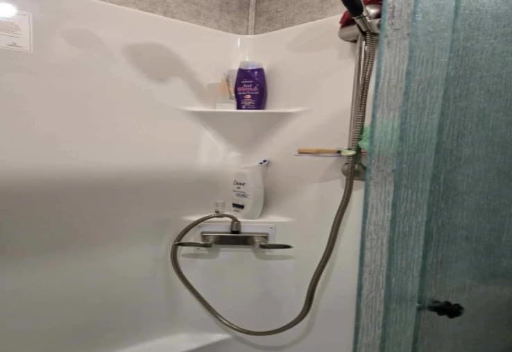 Inside an RV rental: This compact, white shower stall features shelves with toiletries, a flexible shower head, and faucet.