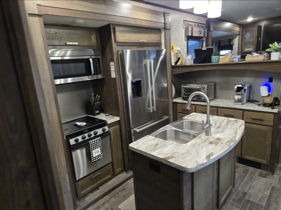 Modern RV rental kitchen features stainless appliances, a double sink island, and ample storage for comfortable travels.