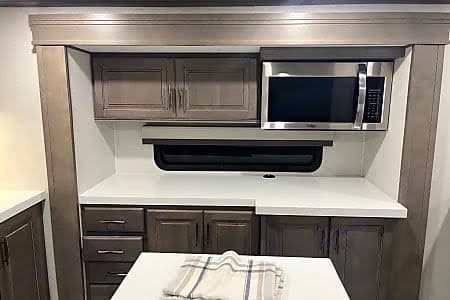 Well-equipped RV rental kitchen: stainless microwave, stylish gray cabinets, and bright white countertops for your travels.