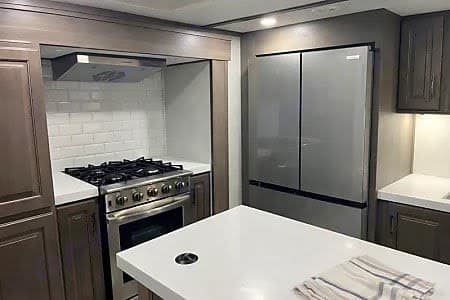 Sleek RV rental kitchen featuring a gas stove, stainless fridge, and white island. Enjoy home comforts on the road.