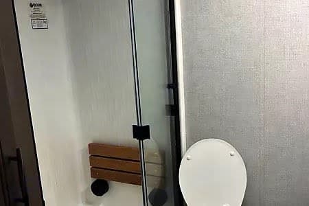 Compact RV rental bathroom featuring a shower with a fold-down seat and a toilet. Ideal for road trips.