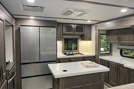 Modern RV rental kitchen interior featuring a stainless steel fridge, dark cabinetry, and white island with ample counter space.
