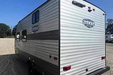 A gray and white Salem FSX travel trailer, seen from the rear and side, ideal for your next RV rental adventure.