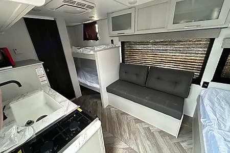 RV rental: Interior shows kitchen (sink, stove), bunk beds, sofa seating, overhead cabinets, and windows with blinds.