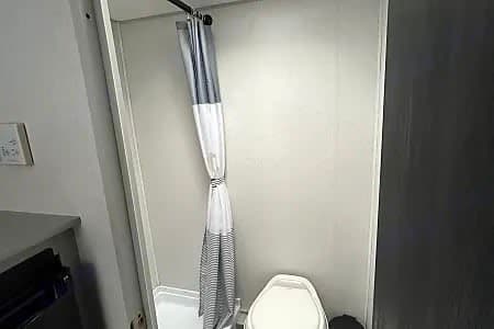 This RV rental bathroom offers a compact shower with a striped curtain and a toilet for your travel comfort.