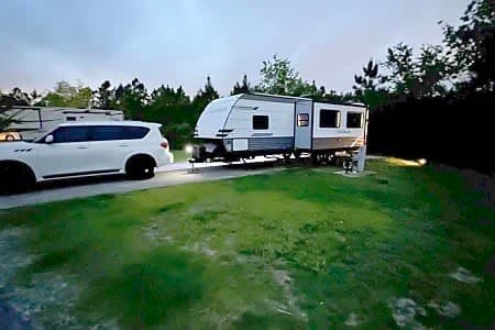 White SUV towing an RV rental at dusk in a campground, ready for outdoor camping adventures.