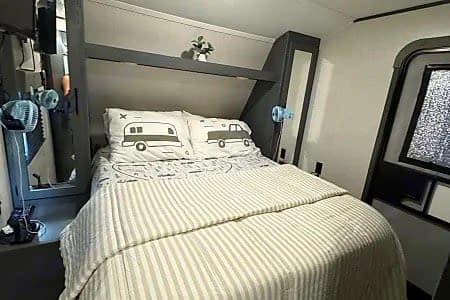 Cozy RV rental bedroom with striped bedding, camper-themed pillows, and a window, ready for your next travel adventure.