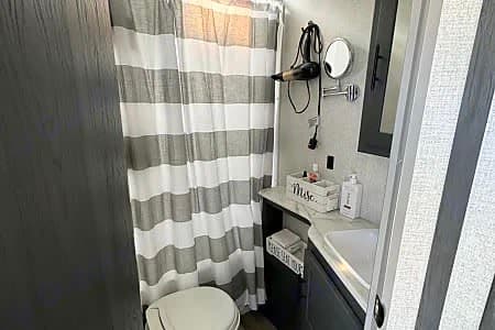 This modern RV rental bathroom features a striped shower, toilet, vanity, mirror, & hairdryer for your comfort.
