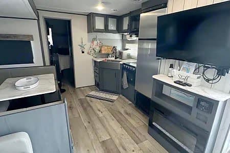 Spacious RV rental interior featuring a modern kitchen, dining booth, and living area with a TV and electric fireplace.