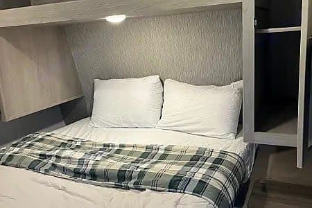 Compact RV rental bedroom with a cozy bed, white pillows, plaid blanket, and convenient built-in storage.