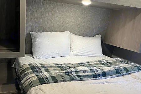 Cozy bed with white pillows and plaid blanket in this RV rental, offering a comfortable sleeping area.