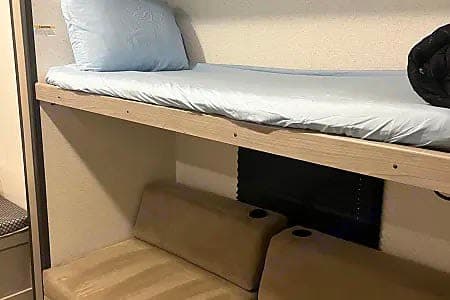 Inside an RV rental: space-saving bunk beds with light blue bedding above tan seating & cup holders below. Compact interior.