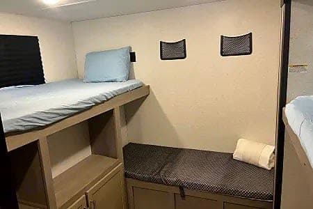 RV rental bunk beds: comfortable sleeping with light blue linens, storage cubbies & mesh wall pockets. Rolled towel on lower bunk.