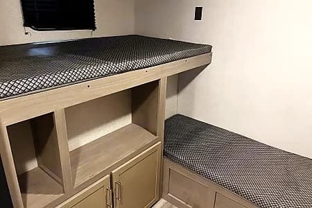 RV rental: Bunk beds with patterned mattresses, built-in storage shelves, and lower seating in a compact, light-toned interior.
