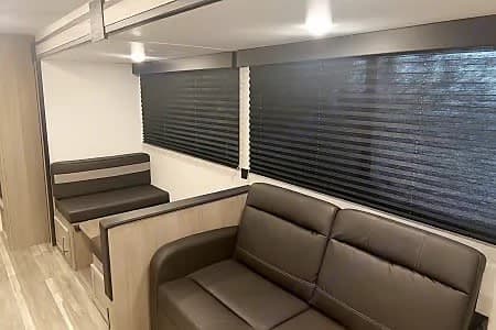 Cozy RV rental interior featuring a dark leather sofa, dinette seating, and privacy blinds on the windows.