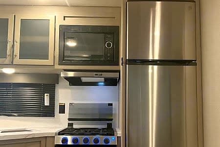 Modern rv rental kitchen with stainless steel appliances including a fridge, microwave, and stove. Perfect for cooking on the road.