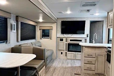 Spacious RV rental interior: living room with TV, kitchen island, dining area with bench seating.