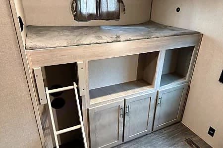 Inside an RV rental: a modern bunk bed with a ladder and built-in storage cabinets, perfect for family adventures.