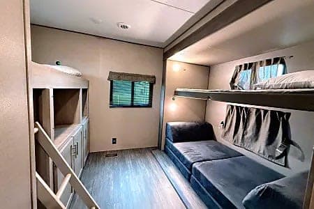 Cozy rv rental with bunk beds, a convertible sofa, and a window. A compact and comfortable sleeping space for families.