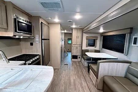 Spacious RV rental interior: modern kitchen with stove/microwave, dining booth, and living area with sofa and light wood tones.