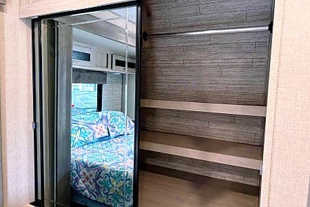 RV rental bedroom closet: mirrored door reflects bed, while interior reveals shelves & a hanging rod for storage.