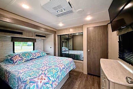 Spacious RV rental bedroom with colorful bedding, mirrored closet, TV, and AC unit, ideal for comfortable travel.