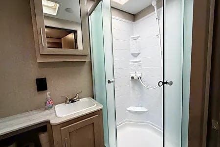 RV rental bathroom: compact vanity with sink & mirror, plus an enclosed shower stall with frosted glass doors.