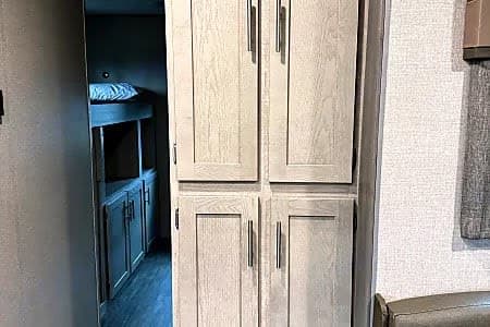 RV rental interior featuring light wood storage cabinets & a glimpse of cozy bunk beds on the left.