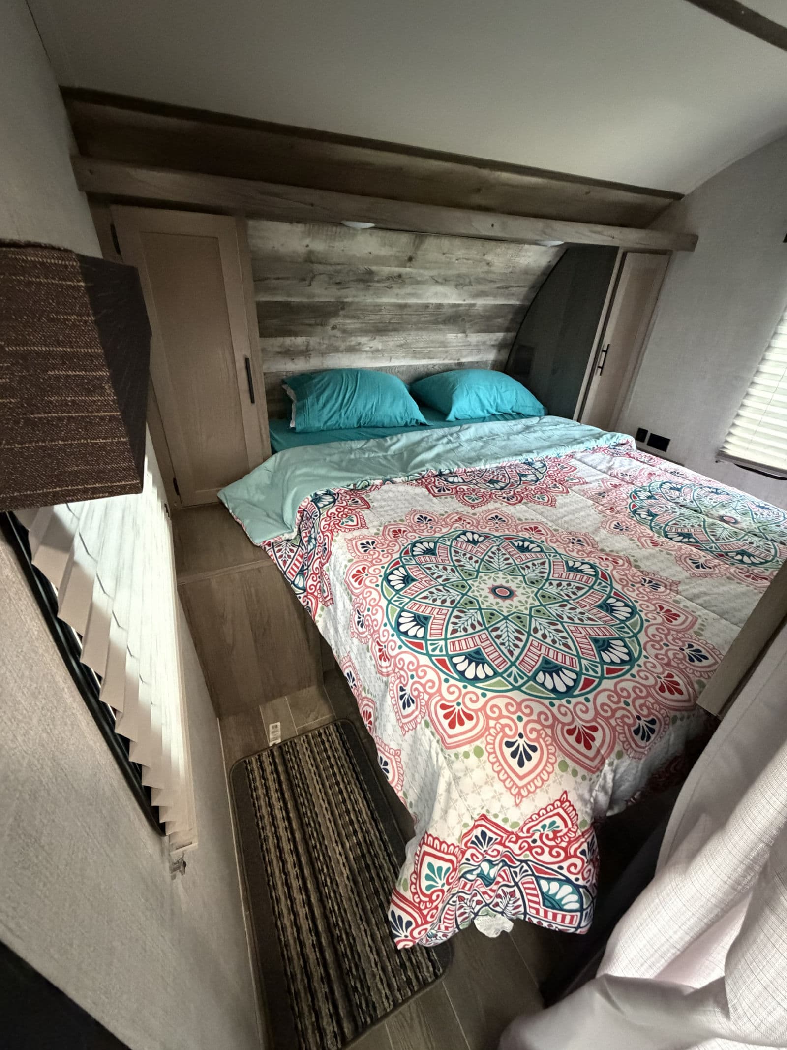 Cozy RV rental bedroom with a vibrant mandala comforter, light blue pillows, wood headboard, and small cabinets.
