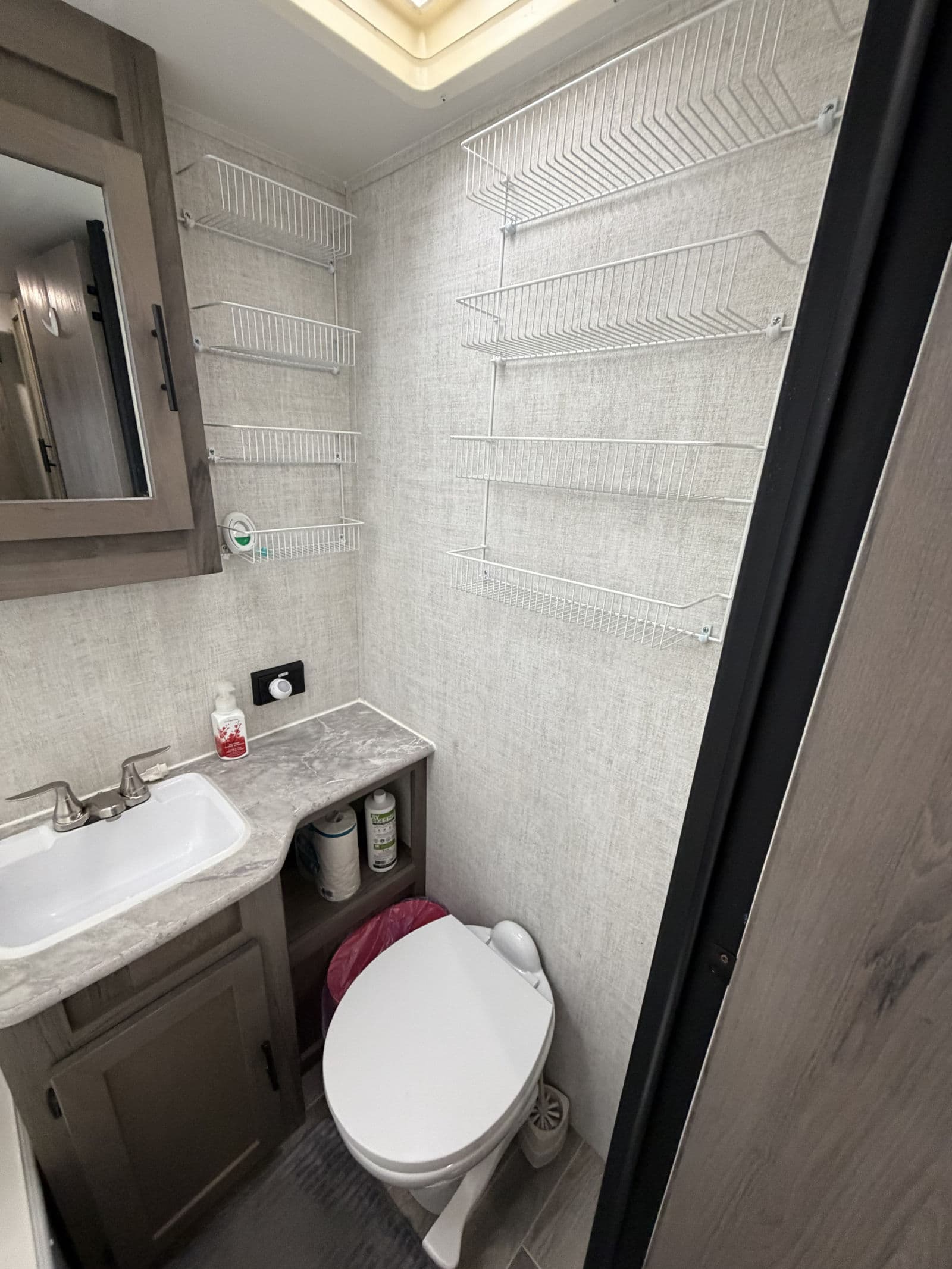 This RV rental bathroom offers a compact sink, toilet, and extensive wall-mounted wire shelves for smart storage solutions.