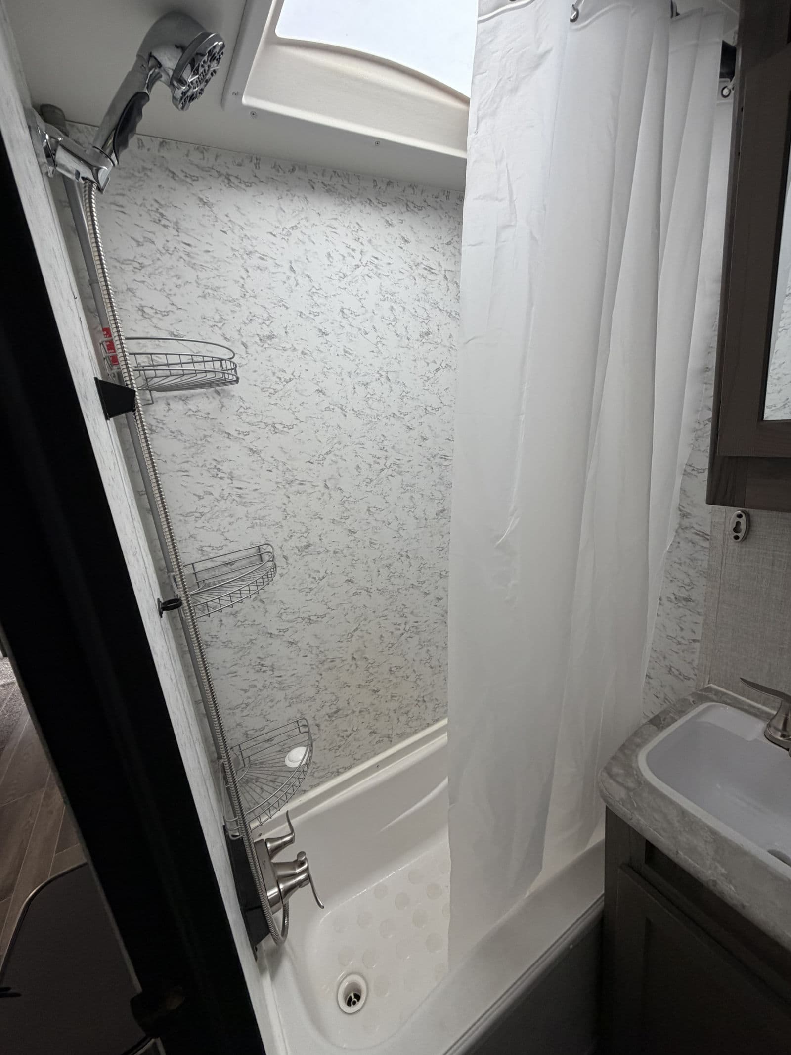 RV rental bathroom with compact shower, handheld showerhead, and sink, perfect for camping trips.