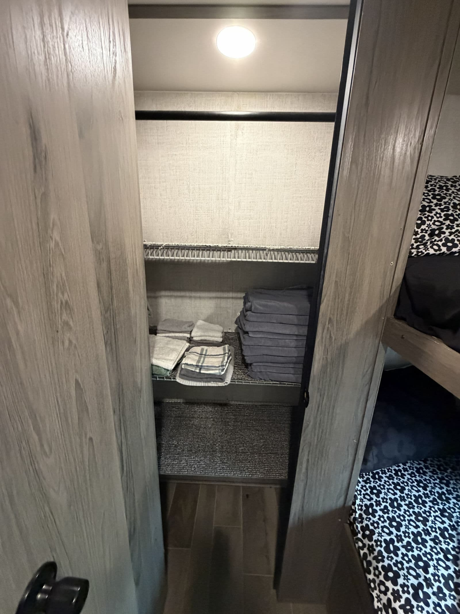 RV rental closet with overhead light, folded towels on a shelf, an empty hanging rod, and adjacent bunk beds.