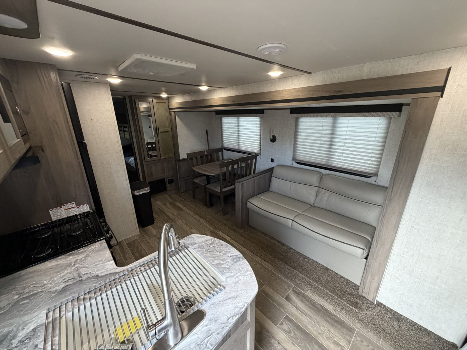 Bright RV rental interior showing living area with sofa, dining table, & kitchen counter with sink & stove.