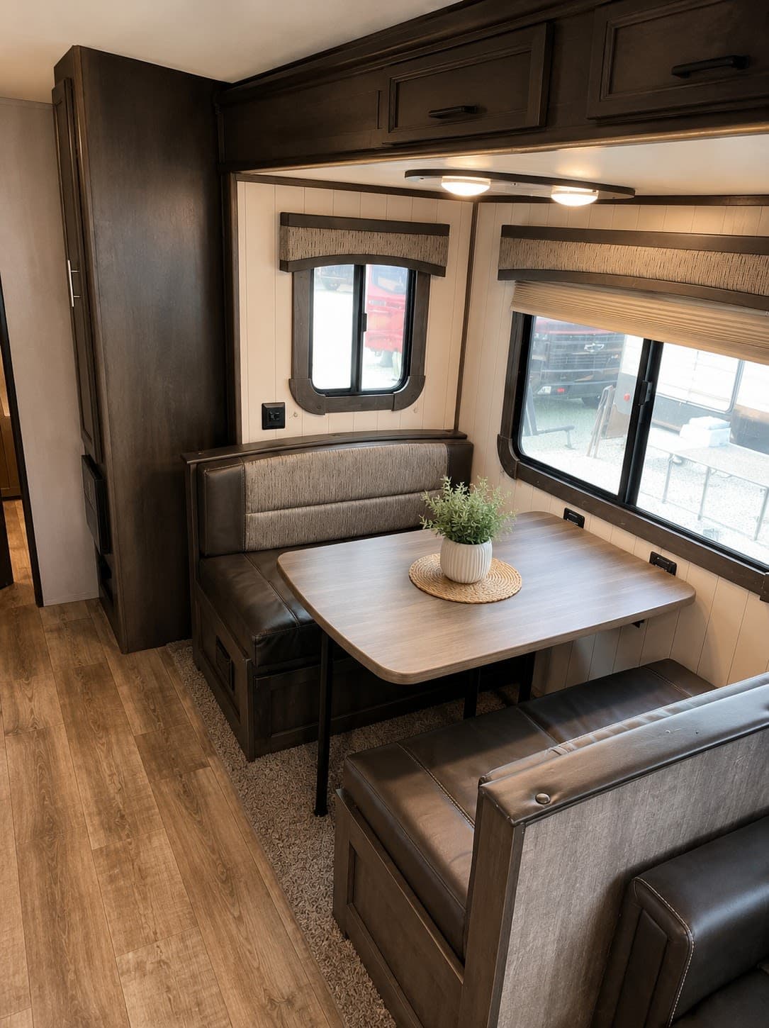 RV rental interior featuring a spacious dinette with comfortable booth seating, a light wood table, and large windows.