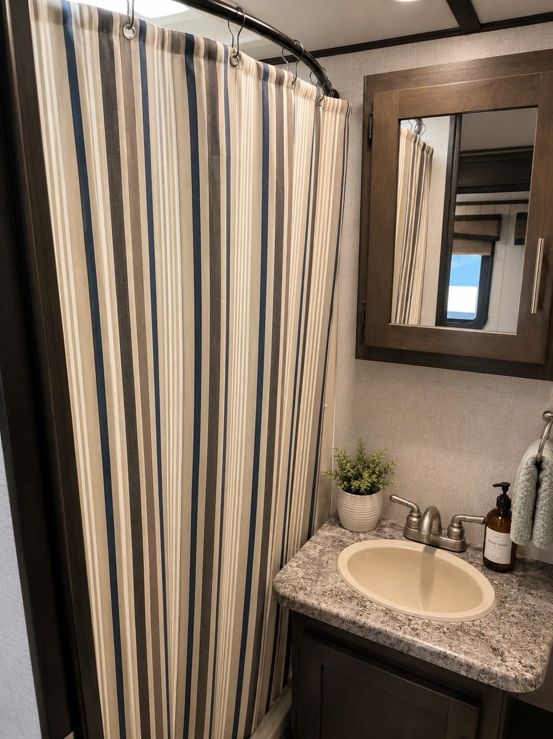 RV rental bathroom with a striped shower curtain, vanity with sink, faucet, and a medicine cabinet mirror. Compact space.