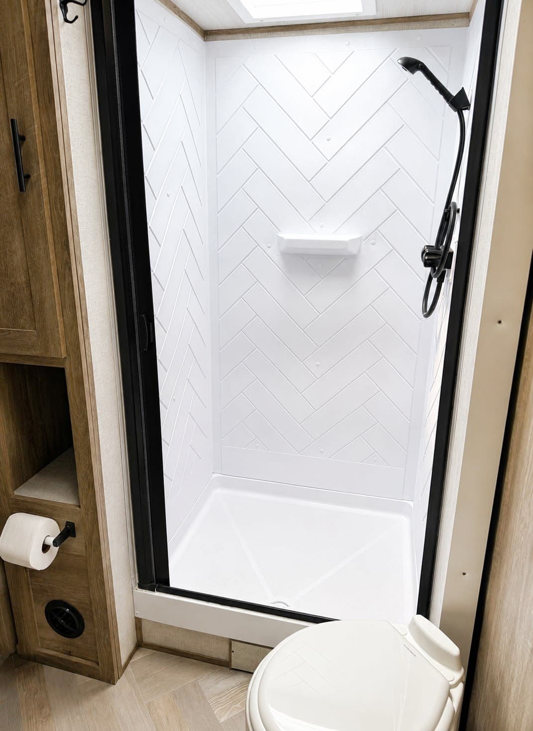 This rv rental features a bright, modern bathroom with a spacious white herringbone shower, toilet, and compact storage.