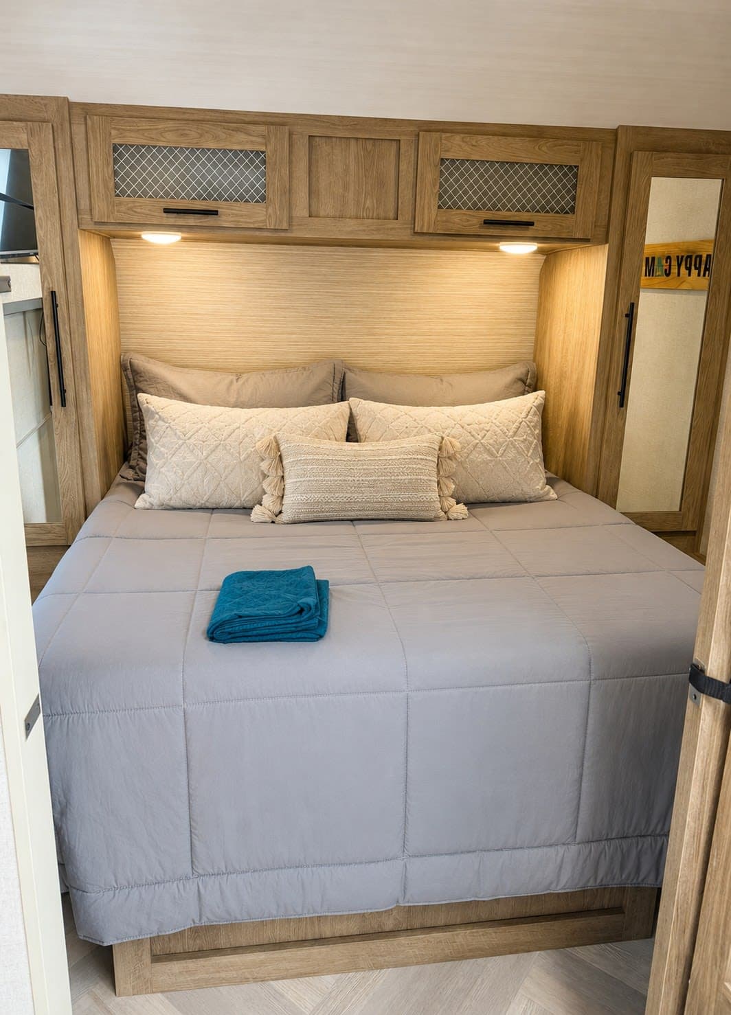 RV rental bedroom with a cozy bed, grey comforter, cream pillows, wood cabinets, and ambient lighting for comfortable travel.