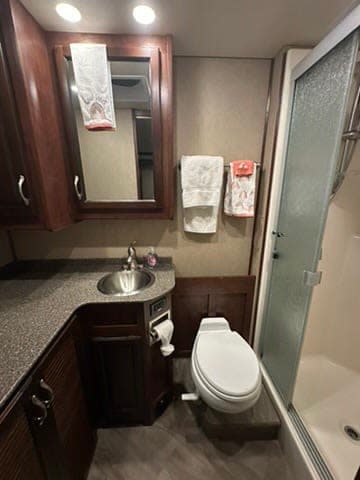 This rv rental bathroom offers a compact design with a sink, mirror, toilet, and glass-enclosed shower, perfect for travel.