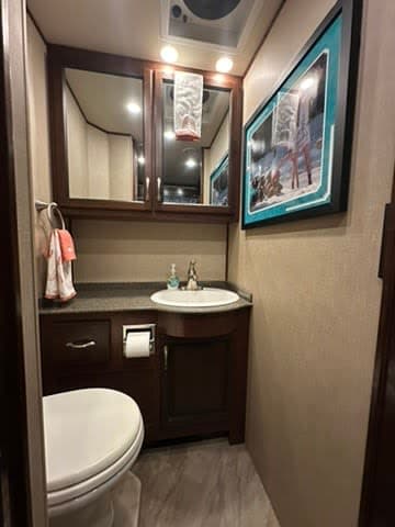Compact and modern bathroom in an RV rental, featuring a toilet, sink, vanity, and mirrored cabinet.
