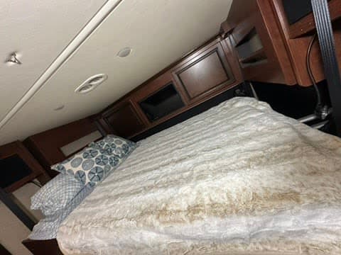 RV rental bedroom with a cozy, fluffy bed & patterned pillows. Overhead cabinets, ceiling lights, & vents provide comfort.