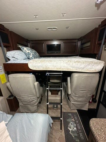RV rental bunk bed sleeping area with a ladder above the front cabin seats, offering compact lodging.