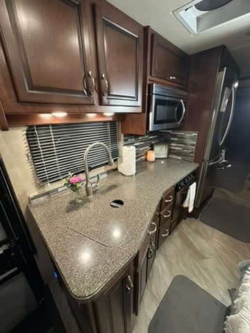 Modern RV rental kitchen: dark wood cabinets, granite-style counters, stainless steel appliances, sink, and stylish backsplash.