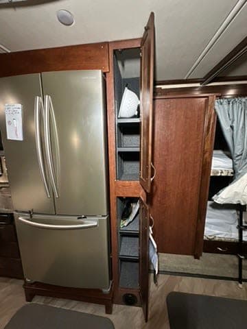 RV rental interior featuring a large stainless steel refrigerator, an open pantry cabinet, and bunk beds.